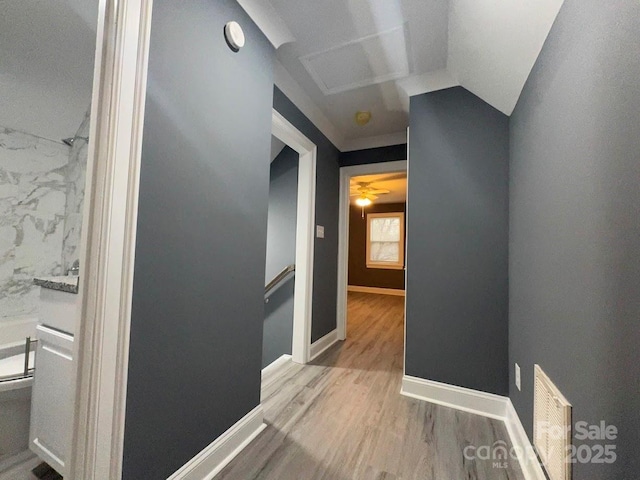 corridor featuring visible vents, baseboards, vaulted ceiling, an upstairs landing, and wood finished floors