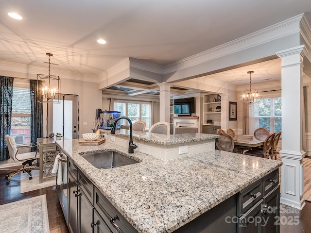 kitchen with ornate columns, dark wood-style flooring, a kitchen island with sink, a sink, and a chandelier