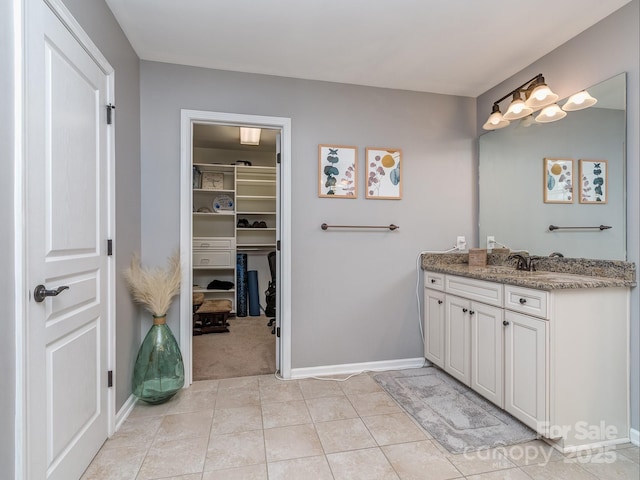 full bath featuring tile patterned floors, vanity, a walk in closet, and baseboards