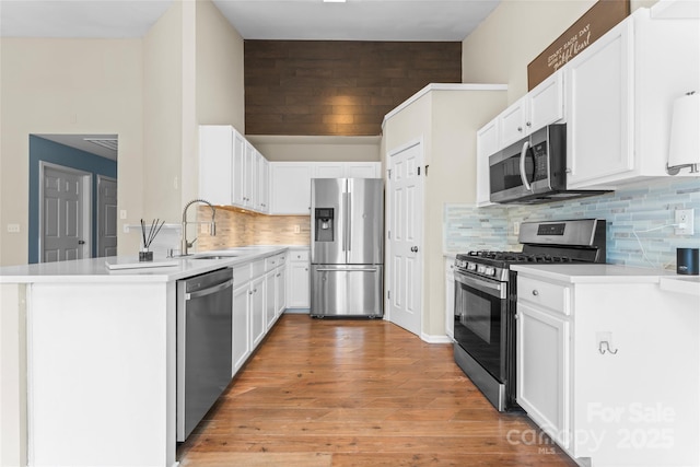 kitchen with a sink, white cabinetry, appliances with stainless steel finishes, a peninsula, and light countertops