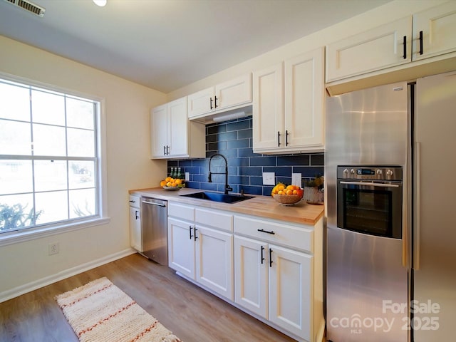 kitchen featuring visible vents, a sink, tasteful backsplash, stainless steel appliances, and light wood-style floors