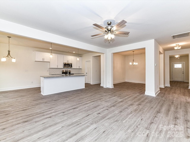 kitchen featuring stainless steel microwave, visible vents, open floor plan, light wood-style floors, and white cabinetry