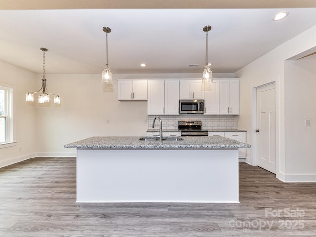 kitchen featuring light wood finished floors, decorative backsplash, appliances with stainless steel finishes, white cabinets, and a sink