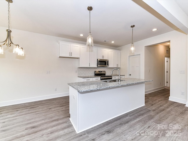 kitchen featuring light wood finished floors, a sink, decorative backsplash, stainless steel appliances, and white cabinetry