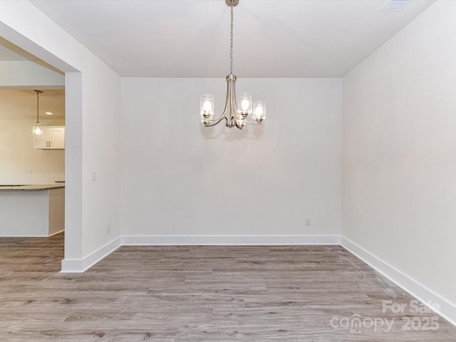 spare room with a chandelier, baseboards, and wood finished floors