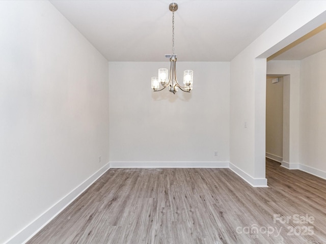 unfurnished room with a notable chandelier, light wood-style flooring, and baseboards