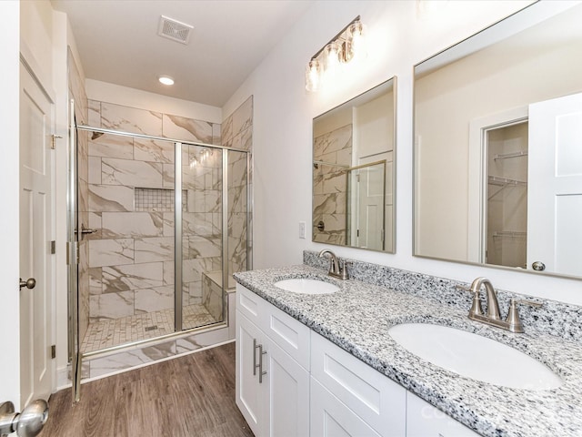 bathroom with a sink, visible vents, wood finished floors, and a shower stall