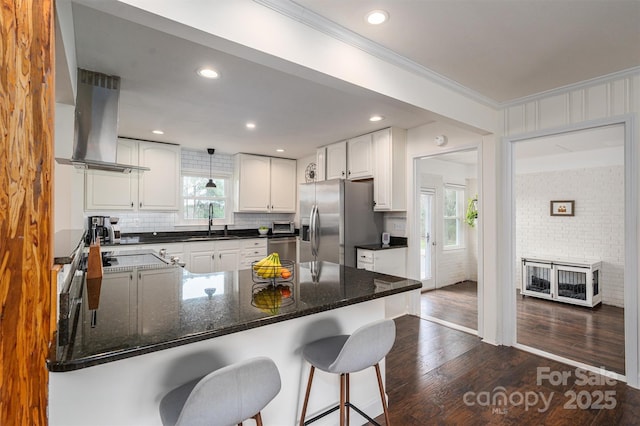 kitchen with dark wood finished floors, a peninsula, island exhaust hood, stainless steel fridge, and a sink