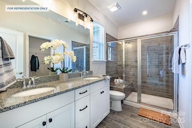 full bath with a sink, wood tiled floor, a stall shower, and double vanity