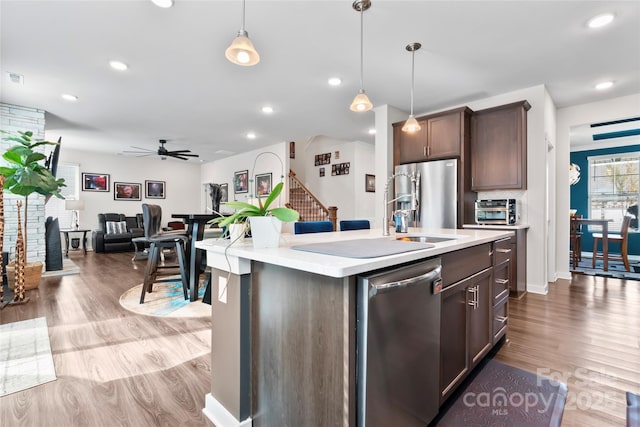 kitchen with wood finished floors, stainless steel appliances, hanging light fixtures, light countertops, and dark brown cabinetry