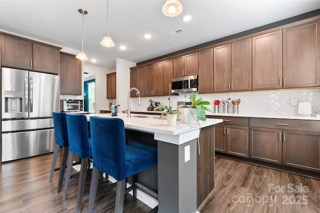 kitchen featuring visible vents, a center island with sink, dark wood-style floors, appliances with stainless steel finishes, and a breakfast bar area