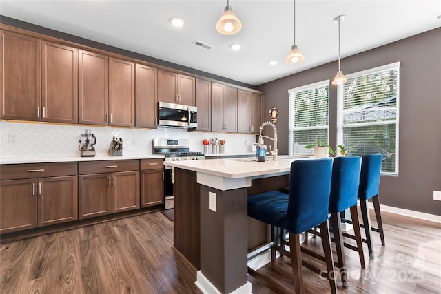 kitchen featuring visible vents, dark wood finished floors, a breakfast bar, decorative backsplash, and appliances with stainless steel finishes