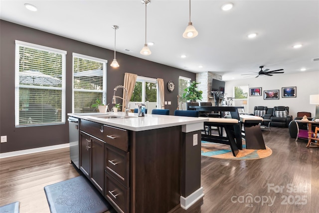 kitchen with a sink, dark brown cabinetry, dark wood-type flooring, stainless steel dishwasher, and open floor plan