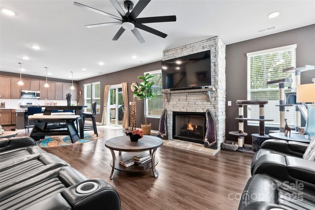 living area with visible vents, a healthy amount of sunlight, a stone fireplace, and dark wood-style flooring