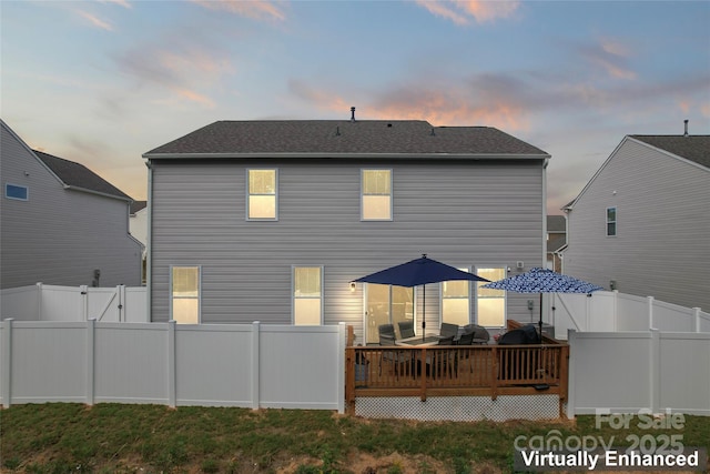 back of house at dusk with a wooden deck and a fenced backyard