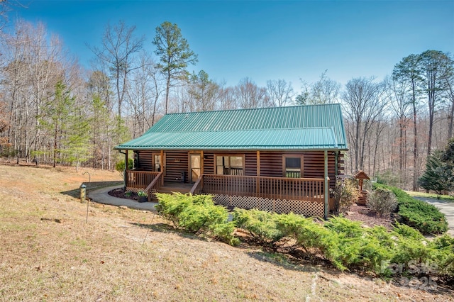 cabin with covered porch, a wooded view, log exterior, and metal roof