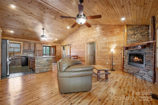 living room featuring ceiling fan, a stone fireplace, and light wood-style flooring
