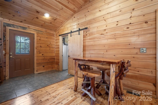 dining room with lofted ceiling, wooden walls, a barn door, wood ceiling, and water heater
