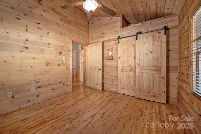 spare room featuring wood ceiling, ceiling fan, wood walls, a barn door, and light wood-style flooring