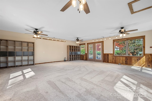 unfurnished living room with ceiling fan, wood walls, track lighting, a wainscoted wall, and carpet flooring