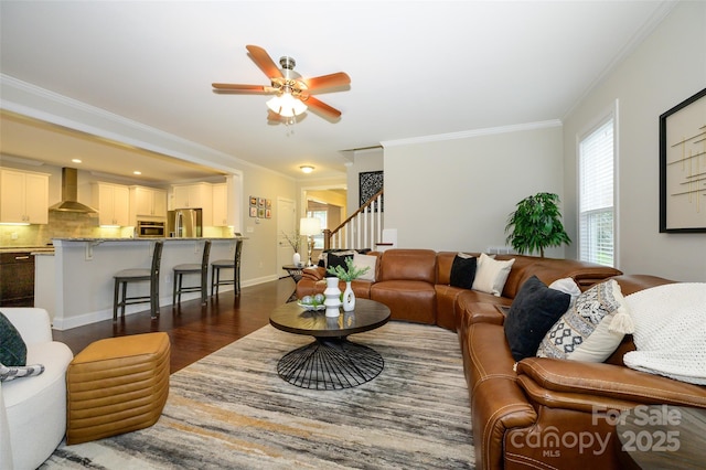 living room featuring crown molding, baseboards, ceiling fan, stairs, and dark wood-style floors