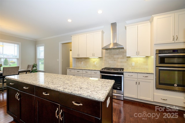 kitchen with a kitchen island, ornamental molding, appliances with stainless steel finishes, dark wood-style floors, and wall chimney exhaust hood