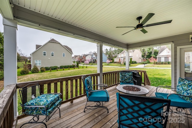 deck with a residential view, a fire pit, ceiling fan, and a lawn