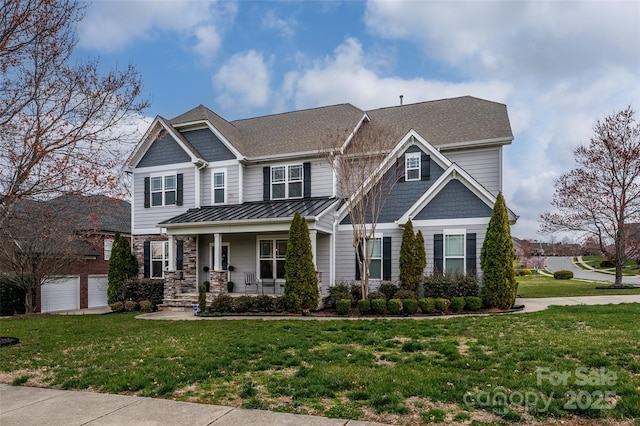 craftsman-style home with a standing seam roof, covered porch, a shingled roof, a front lawn, and stone siding