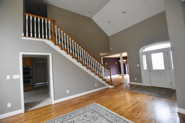 entryway with stairs, wood finished floors, baseboards, and high vaulted ceiling