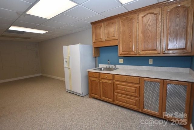 kitchen with brown cabinetry, a sink, light countertops, and white fridge with ice dispenser