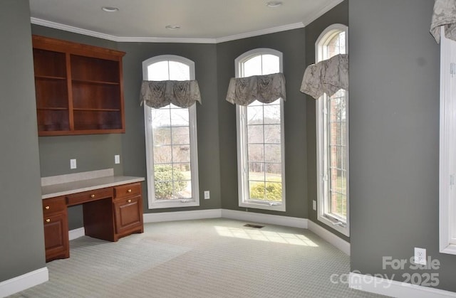 unfurnished office with a wealth of natural light, light carpet, built in desk, and crown molding