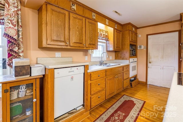 kitchen with light wood-type flooring, light countertops, brown cabinetry, white appliances, and a sink