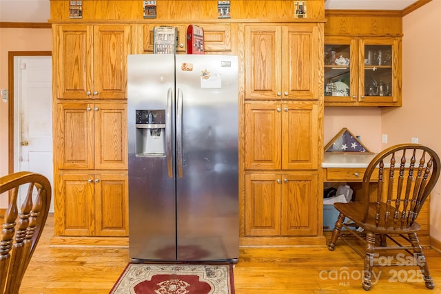 kitchen with light wood finished floors, glass insert cabinets, crown molding, and stainless steel refrigerator with ice dispenser