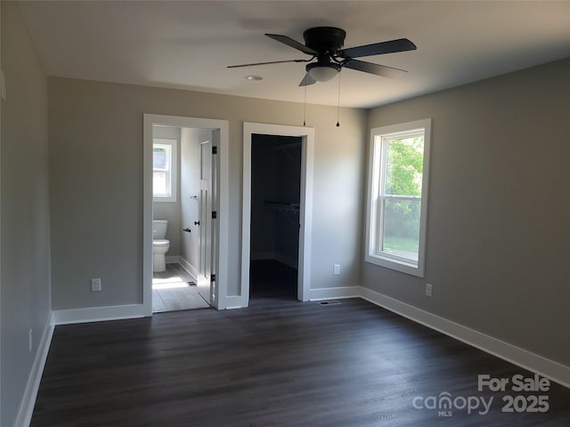 unfurnished bedroom with a walk in closet, baseboards, connected bathroom, and dark wood-style flooring