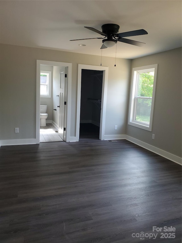 unfurnished bedroom featuring a walk in closet, baseboards, dark wood-type flooring, and ensuite bathroom