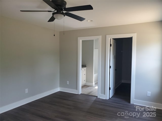 unfurnished bedroom with baseboards, a ceiling fan, wood finished floors, and a spacious closet