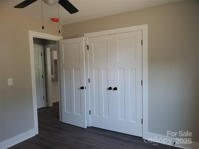 unfurnished bedroom with a closet, baseboards, dark wood-type flooring, and ceiling fan