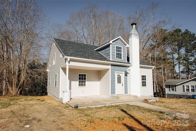 view of front of property featuring a chimney, a front yard, a patio, and a shingled roof