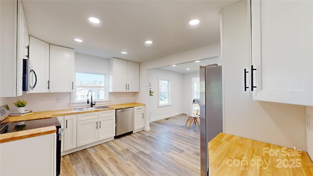 kitchen with wooden counters, light wood-style flooring, appliances with stainless steel finishes, white cabinetry, and a sink