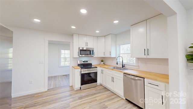 kitchen featuring recessed lighting, butcher block countertops, a sink, white cabinets, and appliances with stainless steel finishes