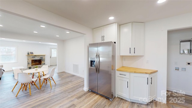 kitchen featuring light wood-type flooring, a stone fireplace, white cabinets, stainless steel fridge, and wood counters