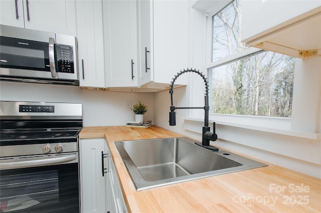 kitchen with a sink, wooden counters, appliances with stainless steel finishes, and white cabinets