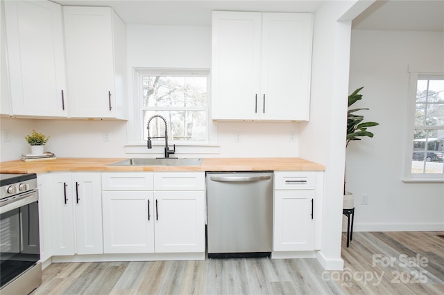 kitchen with light wood finished floors, a sink, stainless steel appliances, wood counters, and white cabinetry