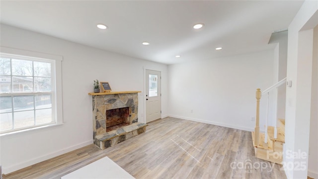 living room featuring recessed lighting, a stone fireplace, wood finished floors, and stairs