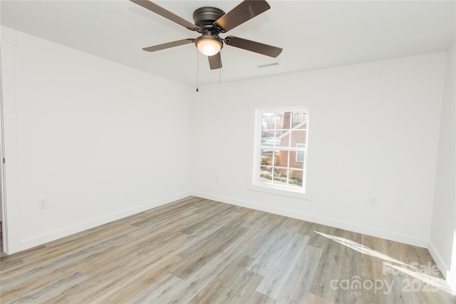 spare room with wood finished floors, visible vents, and baseboards