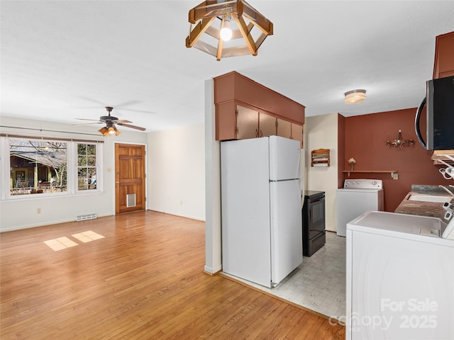 kitchen featuring visible vents, washer and dryer, stainless steel microwave, freestanding refrigerator, and light wood-style floors