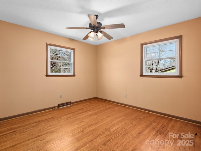 spare room featuring light wood finished floors, visible vents, a ceiling fan, and baseboards