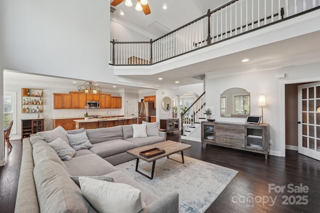 living area featuring dark wood-type flooring, arched walkways, baseboards, a towering ceiling, and stairs