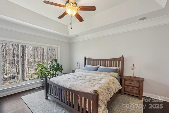 bedroom with baseboards, ornamental molding, wood finished floors, a raised ceiling, and a ceiling fan