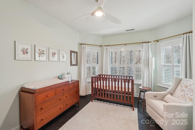 bedroom featuring a ceiling fan, dark wood-style floors, visible vents, baseboards, and a nursery area